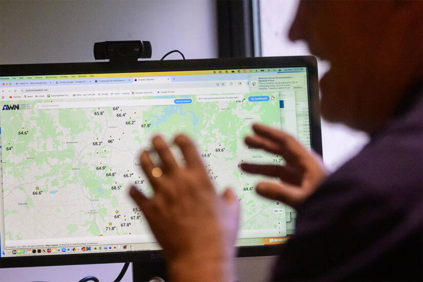 A person in the foreground has his face and hands silhouetted against a computer screen; the screen shows a series of average temperatures spread across a large geographic area.
