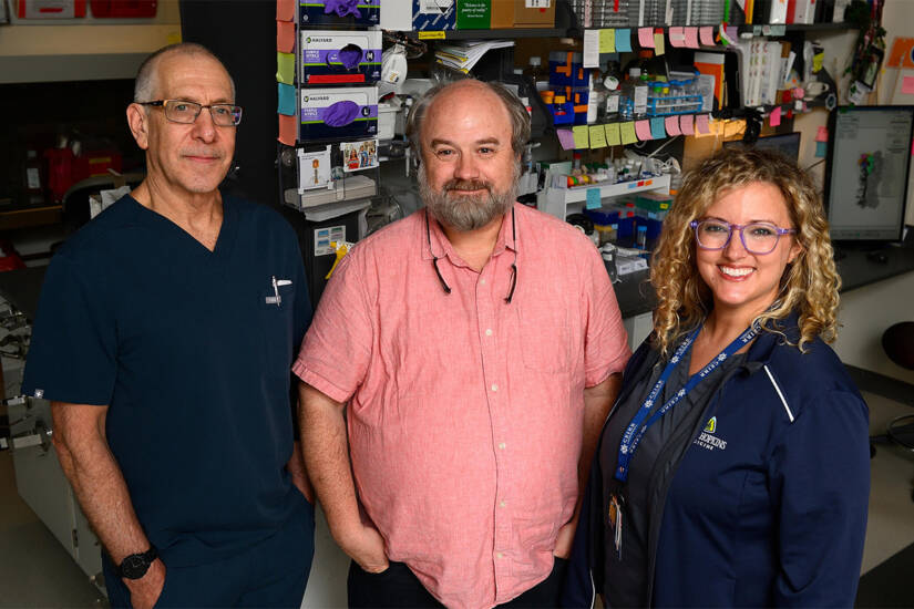 Three people stand shoulder to shoulder, posing for a photo in a lab setting.